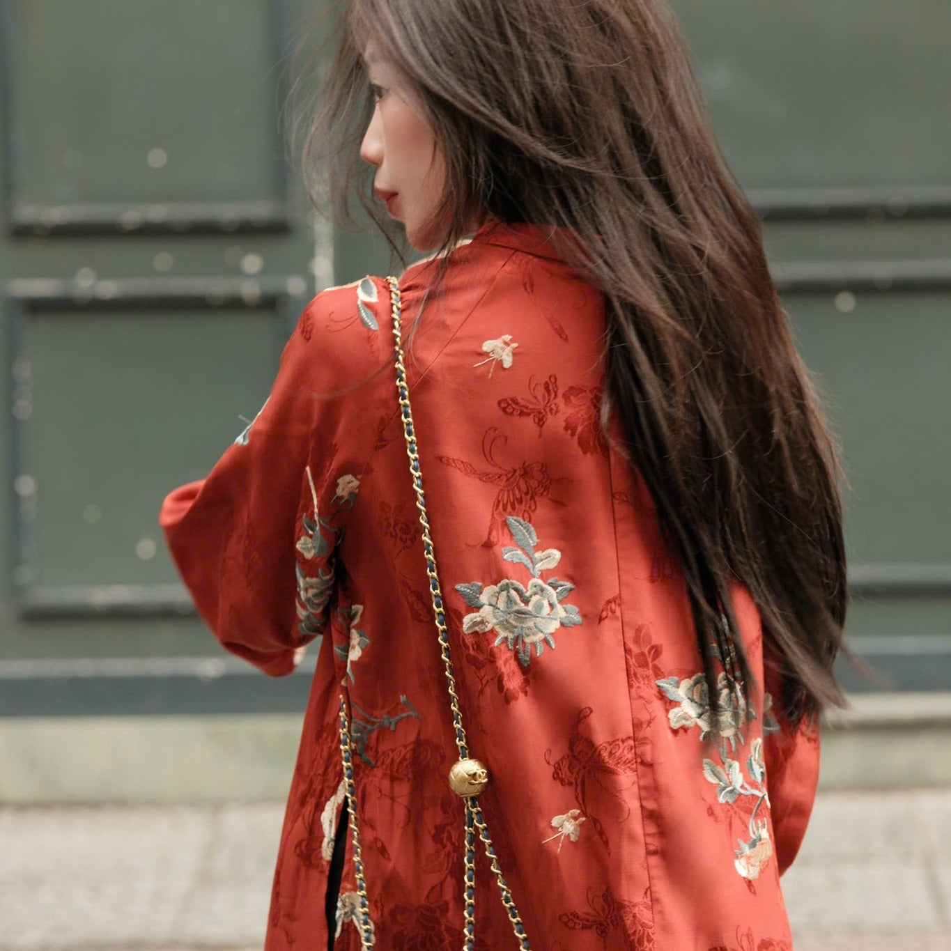 A person wearing a red, floral-embroidered jacket with a crossbody chain bag.