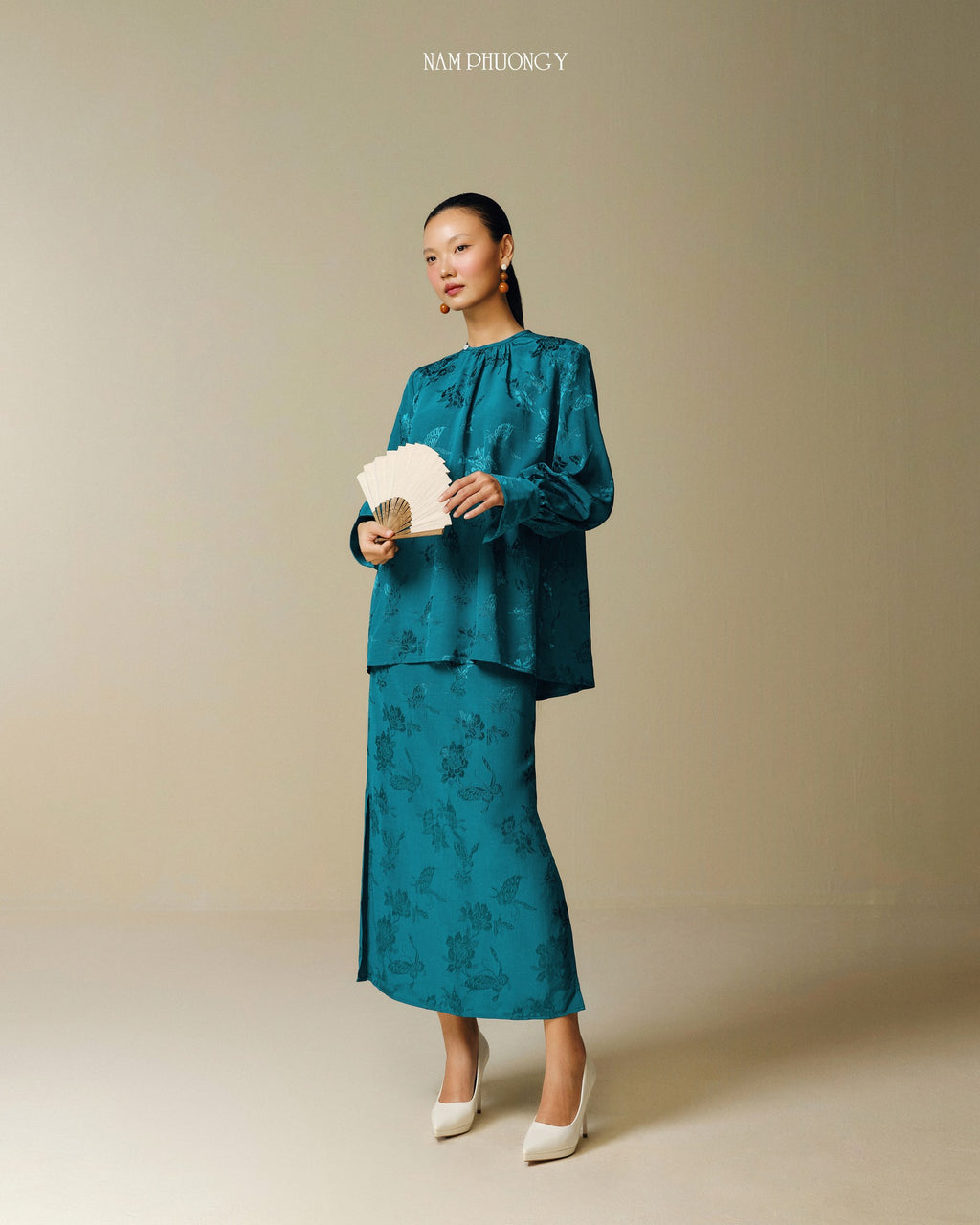 "Traditional Vietnamese dress 'Dong' in dark teal jacquard silk by Nam Phuong Y, blending modern and traditional patterns."