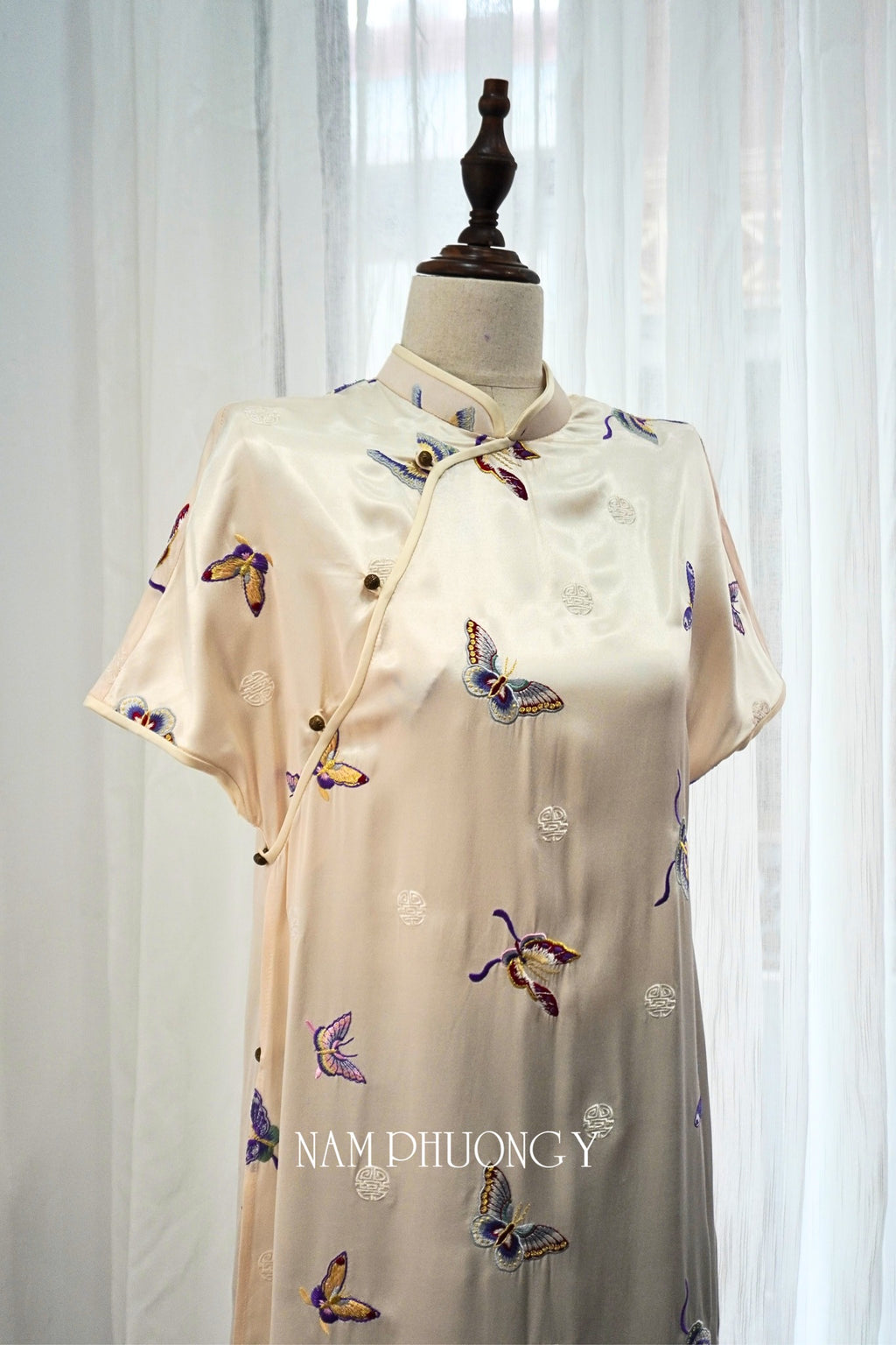 "Tú Điệp" premium short-sleeve embroidered ivory silk Ao Dai by Nam Phuong Y, featuring traditional Vietnamese design with colorful butterfly embroidery.