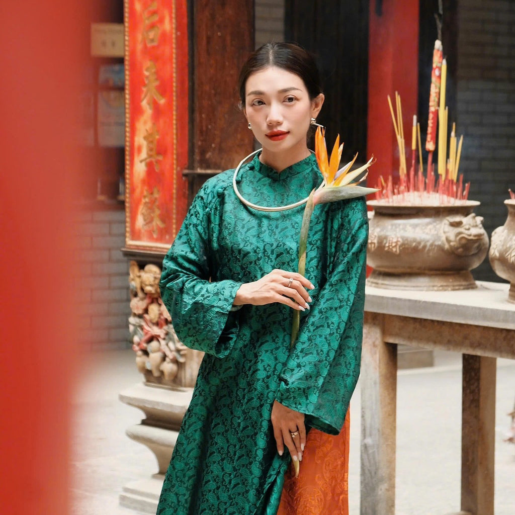 A person wearing a green traditional outfit in a temple setting, holding a bird of paradise flower.