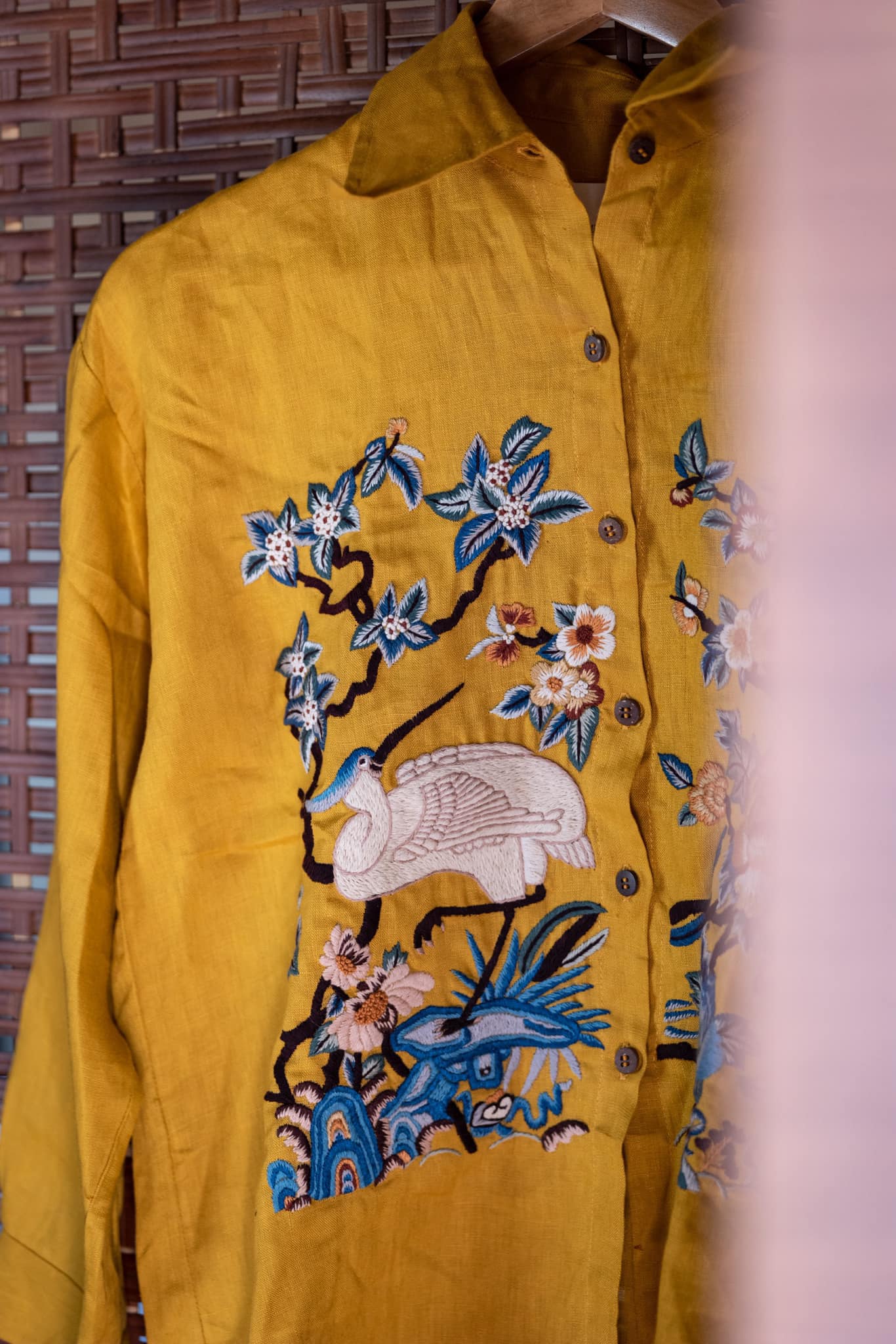 Mustard yellow shirt with intricate embroidery of a white crane, blue and green foliage, and pink flowers.