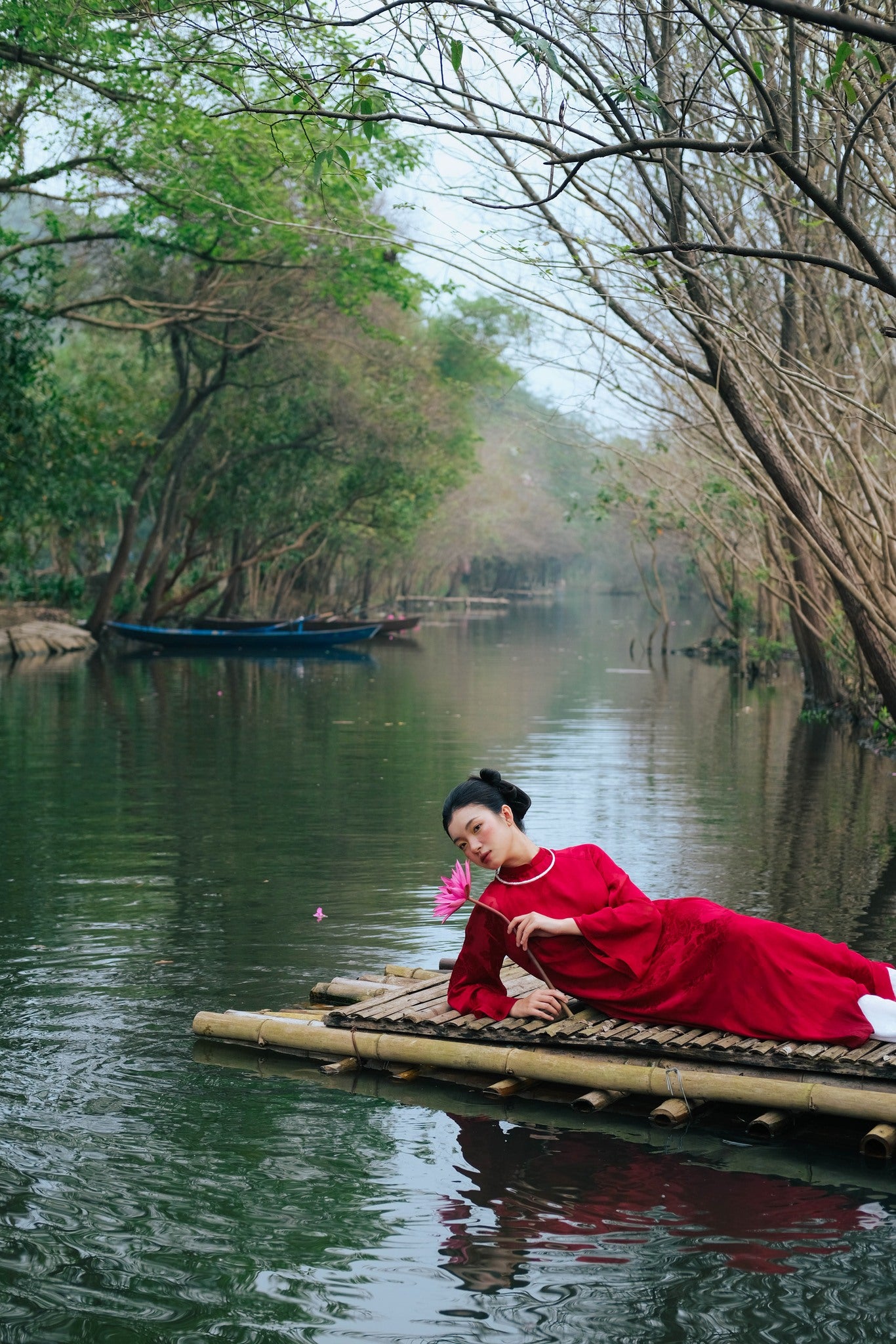 "Traditional Vietnamese Ao dai in crimson silk, artisan-crafted, with flowery design, on a serene river setting."