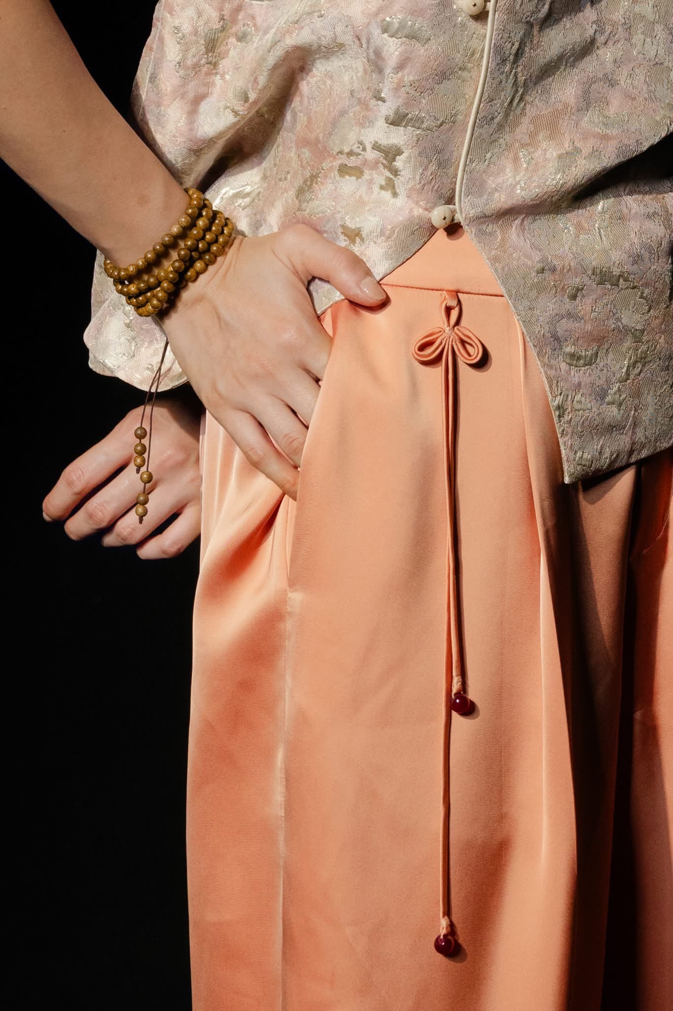"Traditional Vietnamese Nghinh Xuan silk pants in peach orange with tassel, cultural authenticity by Hy Phuong."