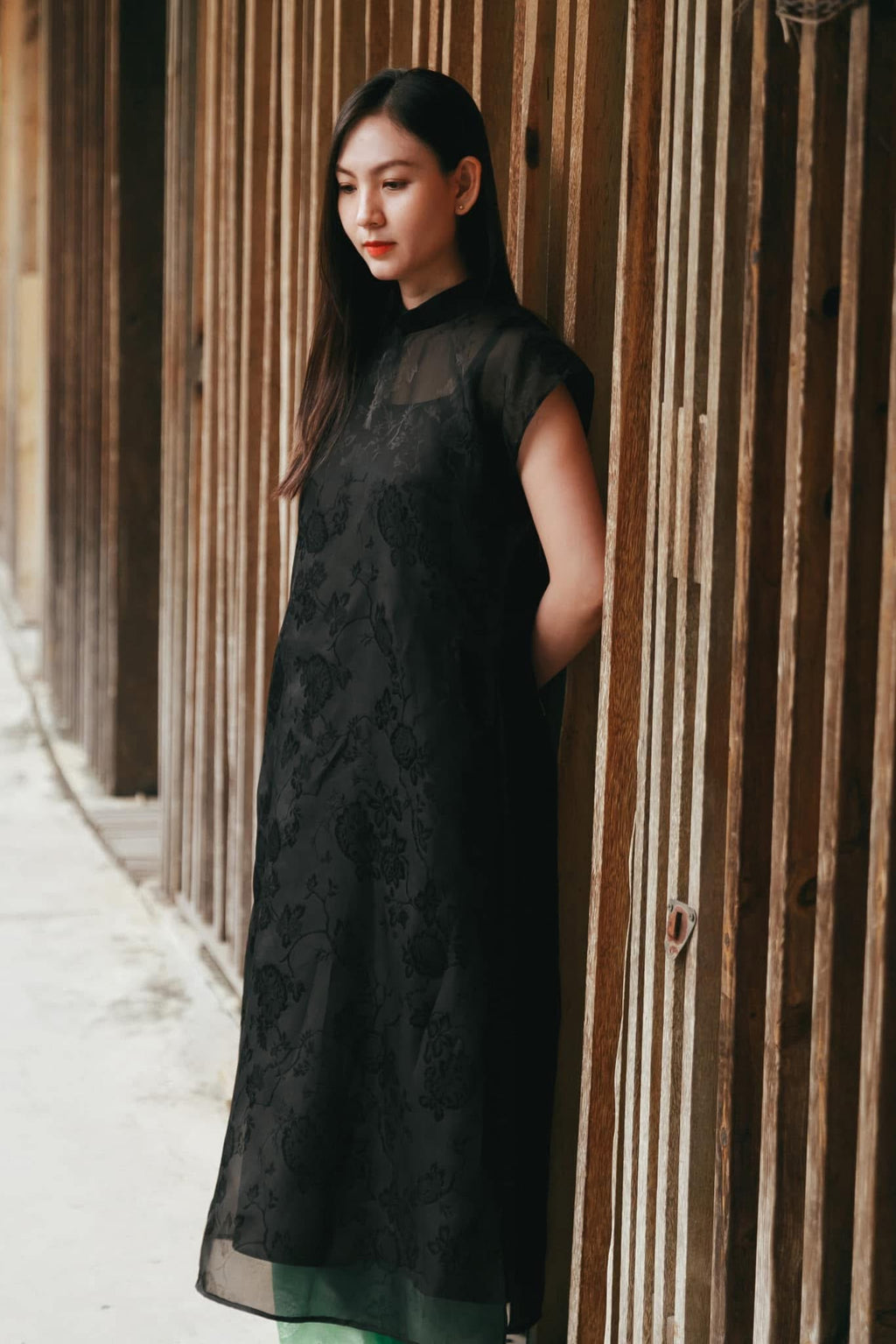 Black sleeveless silk áo dài with floral jacquard detail and green pants - traditional Vietnamese dress by Nam Phuong Y