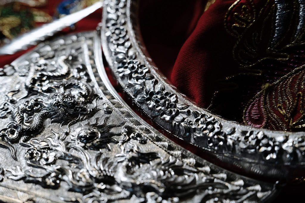 "Traditional 'Nhat Chi Mai' silver collar necklace with floral patterns, red silk background, artisan-crafted."