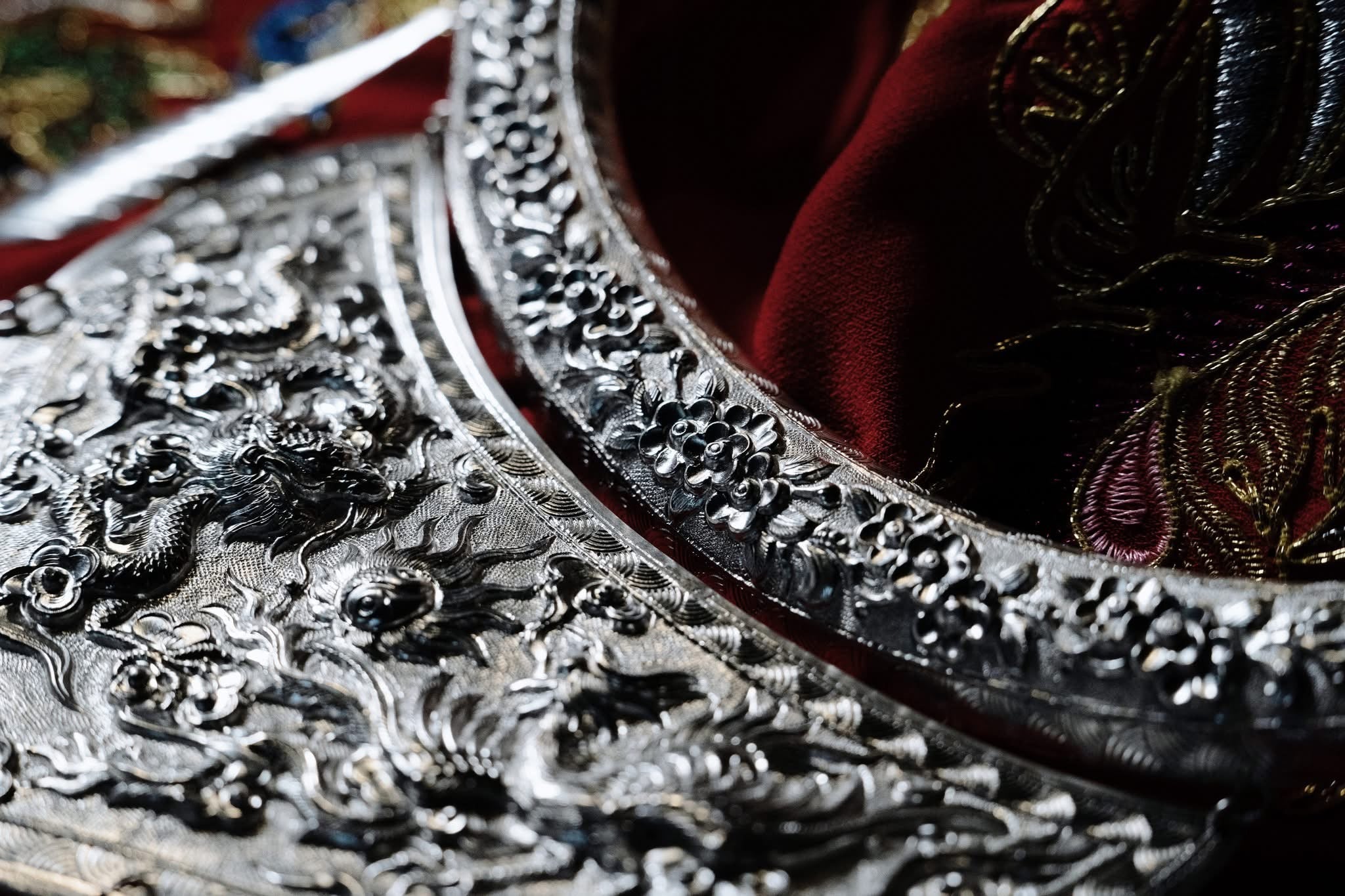 "Traditional 'Nhat Chi Mai' silver collar necklace with floral patterns, red silk background, artisan-crafted."