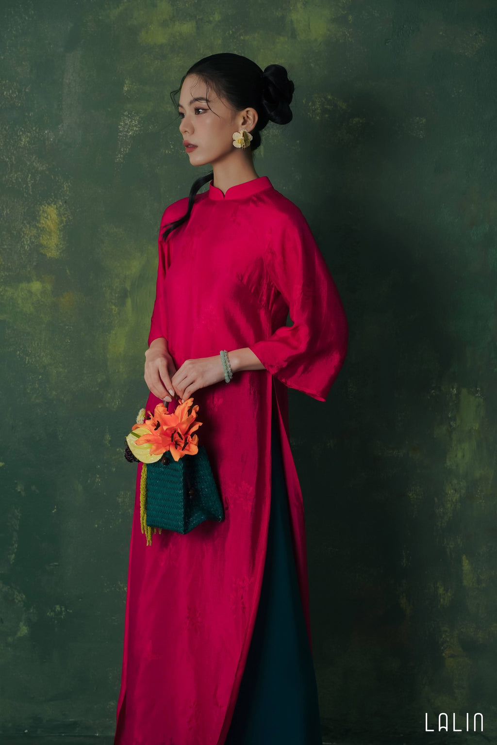 Woman in a bright pink Ao dai holding a colorful flower against a dark green background