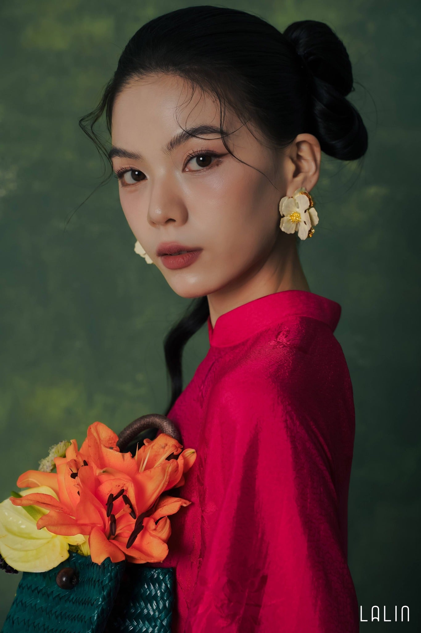 Woman in a red Ao dai holding flowers against a green background