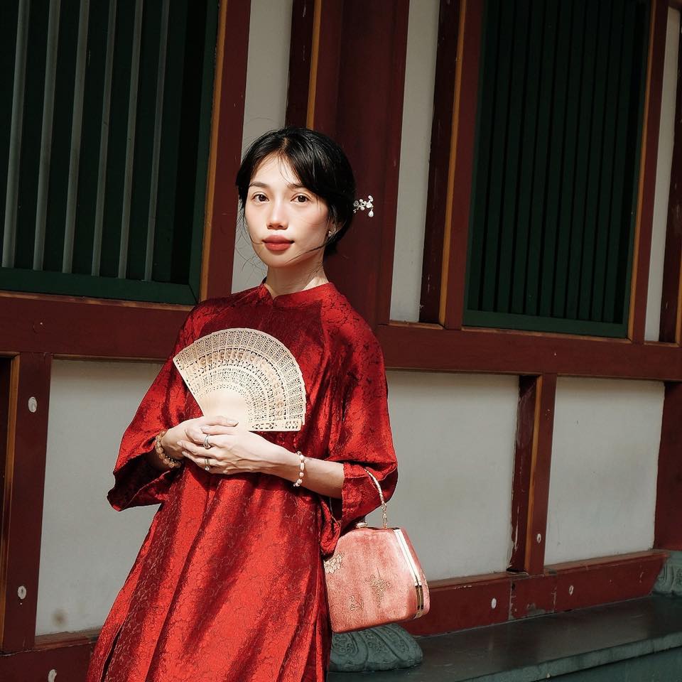A woman in a red traditional outfit holding a decorative fan, with a matching handbag.