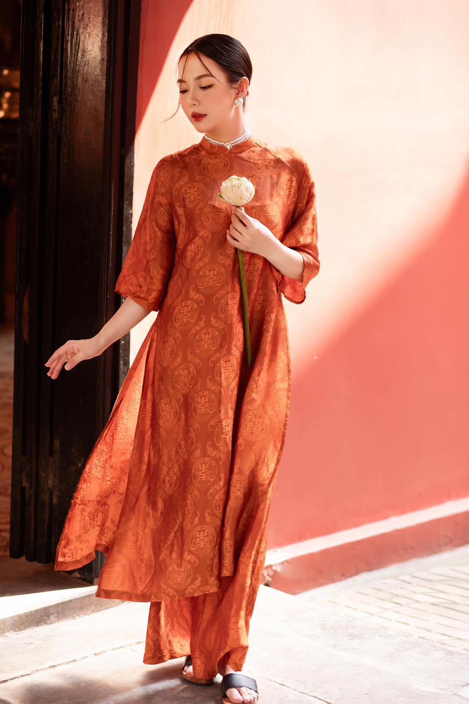 "Tho Doi Ao Dai set in orange wormsilk, traditional Vietnamese dress by Moc, featuring jacquard patterns."
