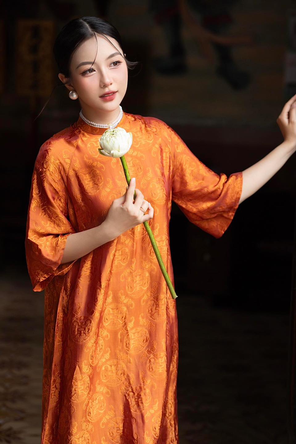 "Tho Doi Ao Dai set in orange wormsilk, traditional Vietnamese dress by Moc, featuring jacquard woven patterns."